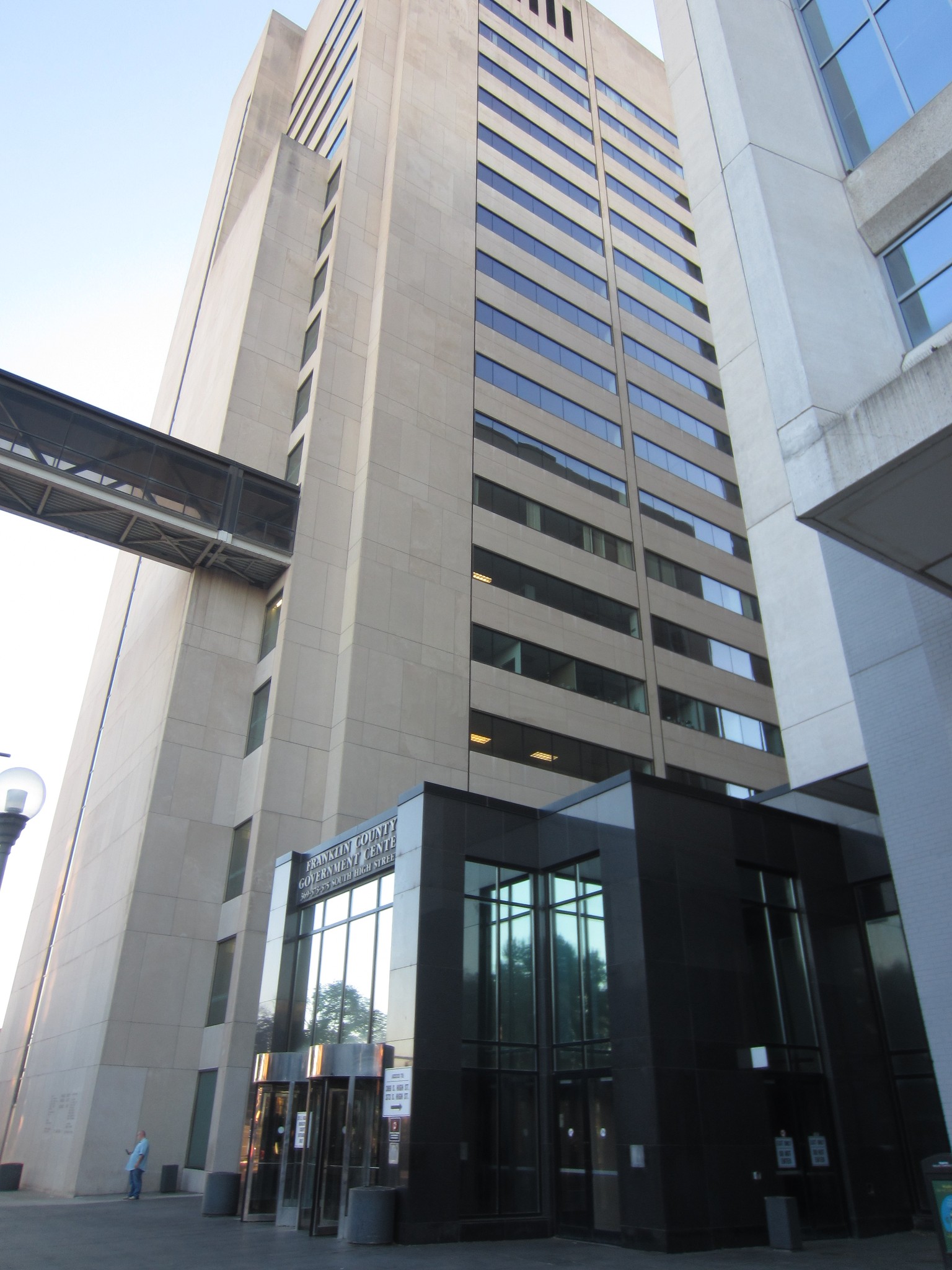 Low-angle view of the Franklin County Municipal Court building at 375 S. High St. in Columbus, Ohio, showing the entrance pavilion with address lettering and an elevated pedestrian skywalk.