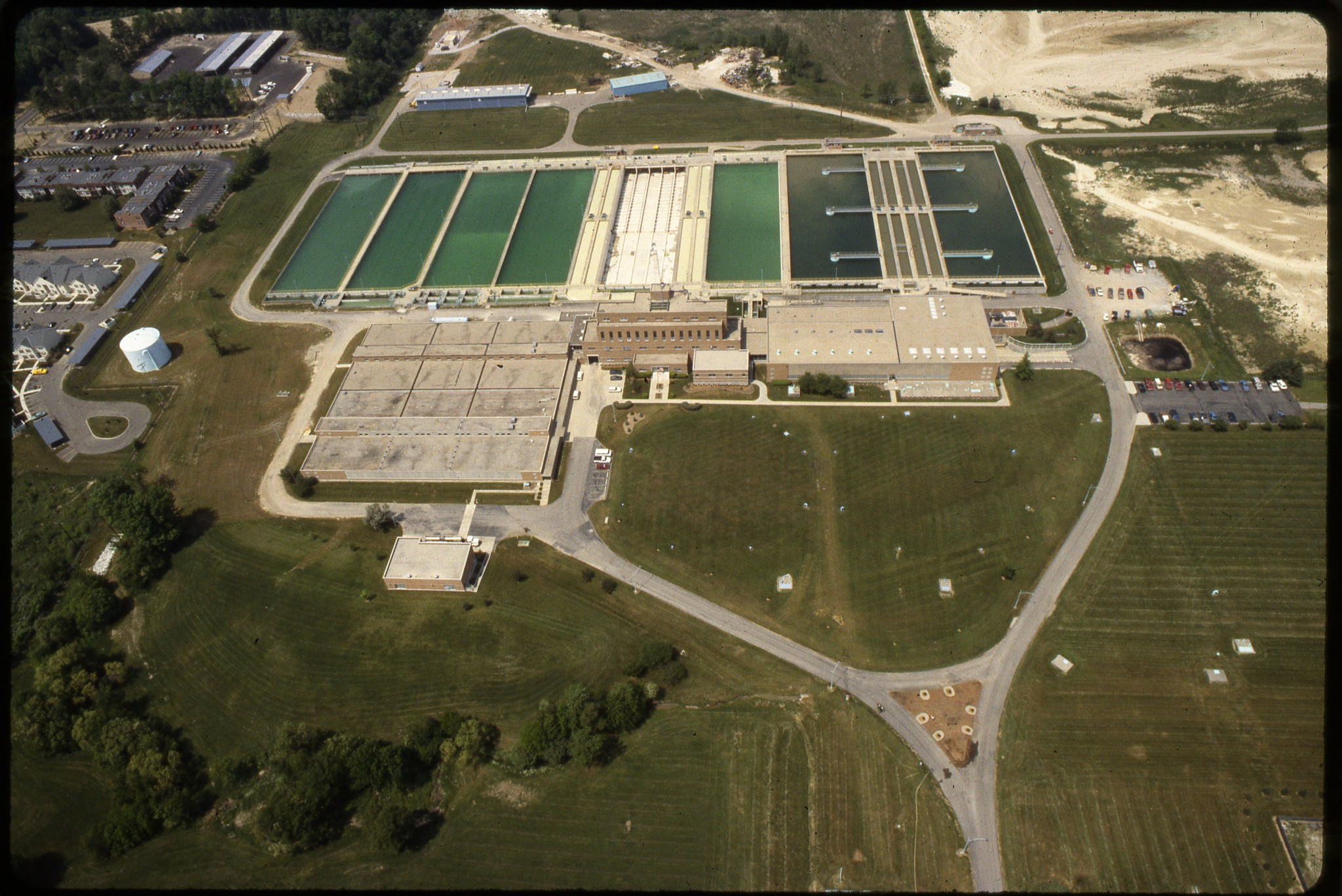 Aerial perspective of the Hap Cremean Water Plant showing multiple large water treatment basins, central brick administrative buildings, and grounds in Columbus, Ohio.