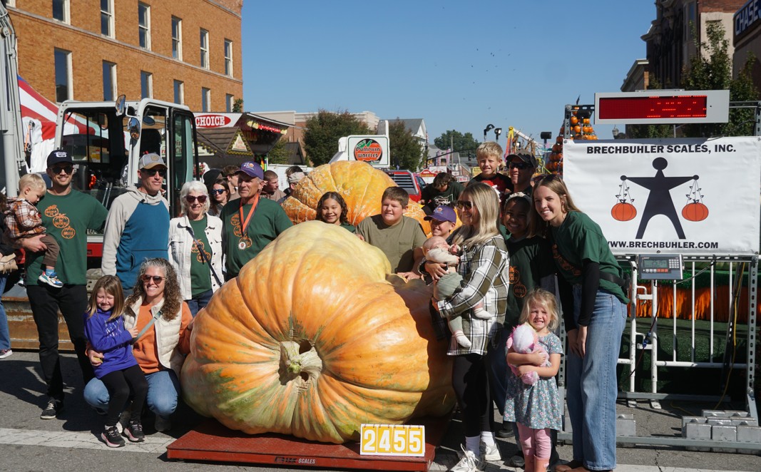 A large family and grower group pose behind a colossal 2,455-pound pumpkin on a Brechbuhler platform scale in downtown Circleville.