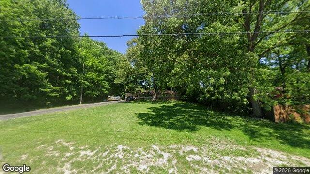 Street-level view of a wide green lawn leading to mature trees and a single-story structure at 1696 N. Hague Ave.