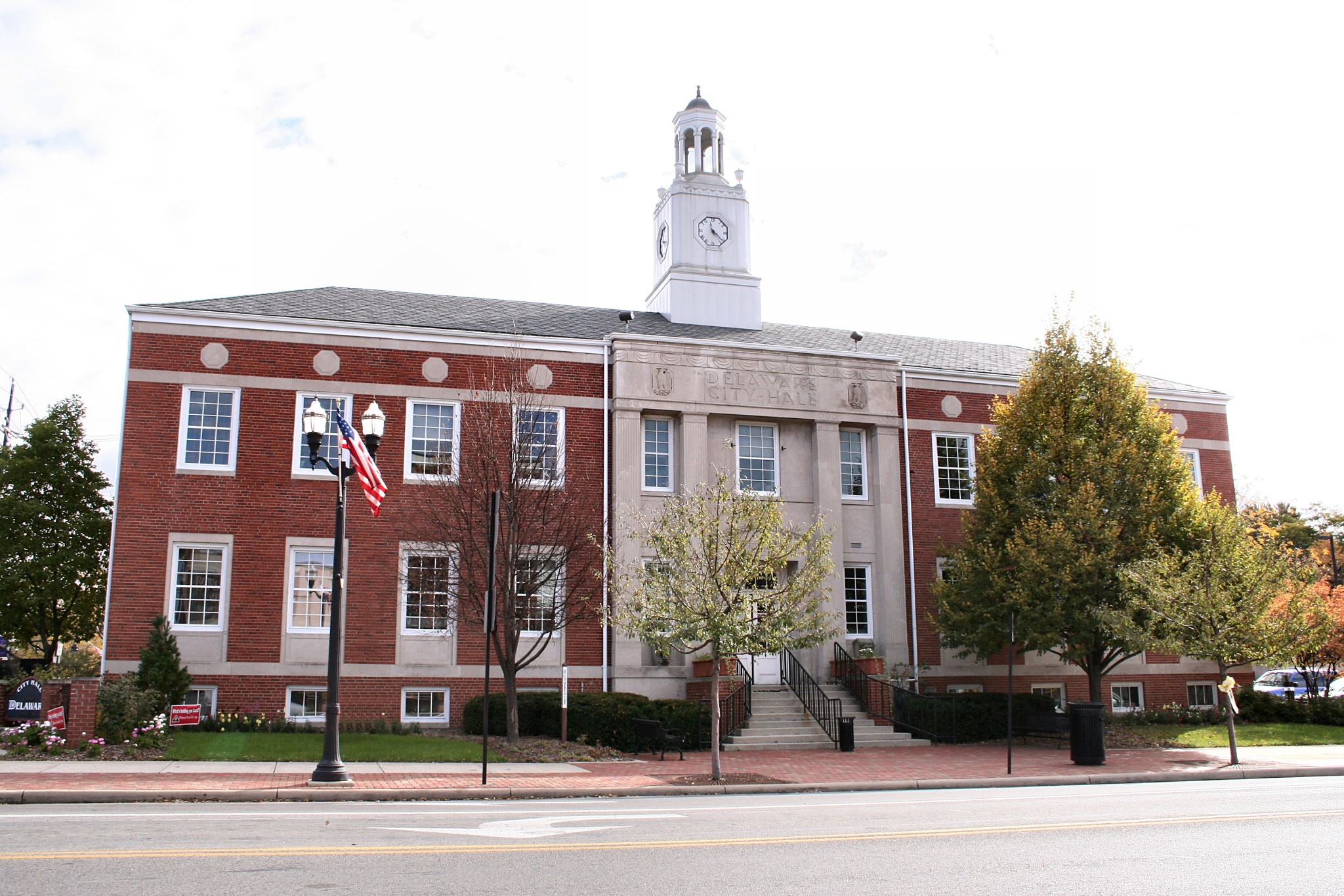Exterior view of Delaware City Hall, a two-story red brick municipal building with a stone entrance portico and clock tower cupola.