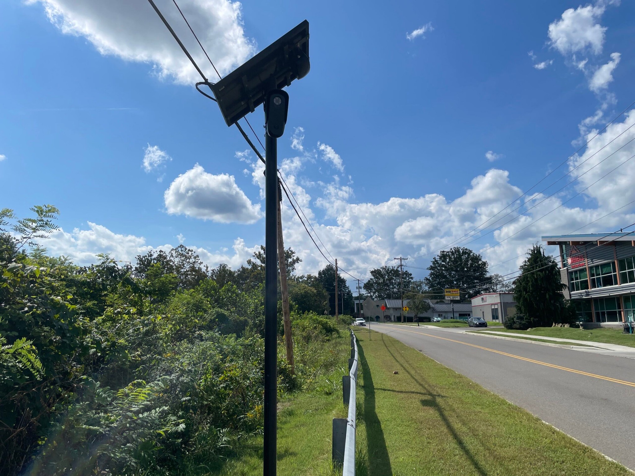 A black Flock Safety license plate reader camera and solar panel on a pole next to a guardrail along West Union Street in Athens, Ohio.