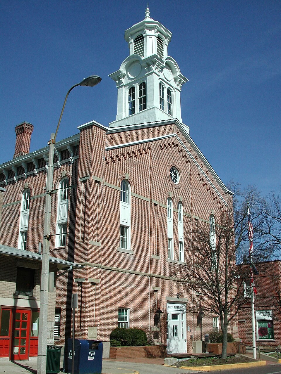 Historic red brick Athens City Hall building with a white bell tower cupola, arched windows, and 'CITY BUILDING' inscribed above the entrance under a clear blue sky.