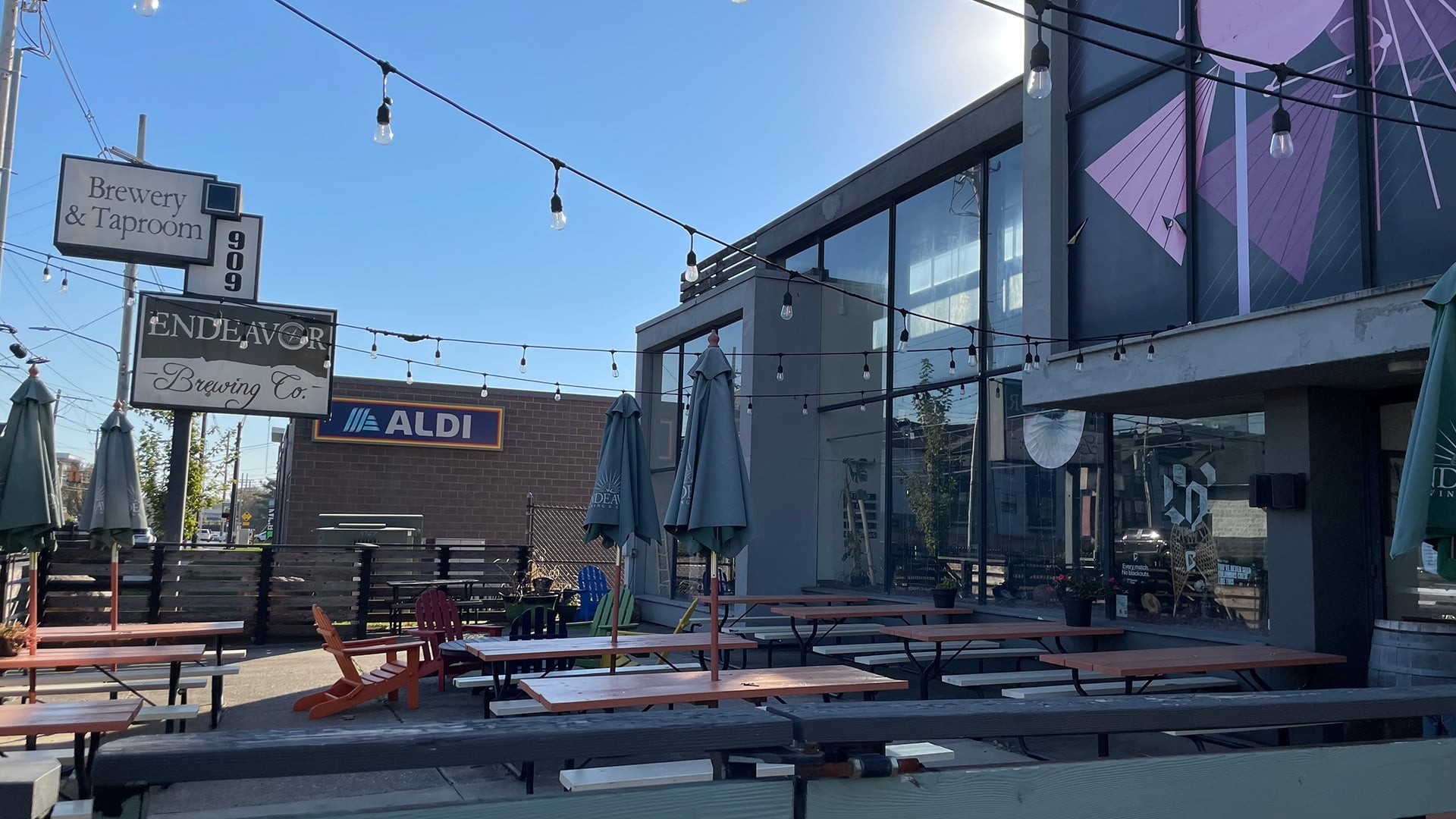Outdoor patio of Endeavor Brewing & Spirits with picnic tables, string lights, and a sign reading Brewery & Taproom 909 Endeavor Brewing Co.
