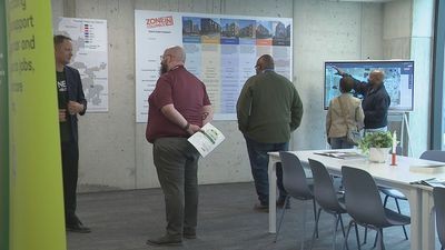 Wide view of the Zone In Gallery interior in Columbus, showing residents reviewing zoning maps and display panels while conversing with staff.