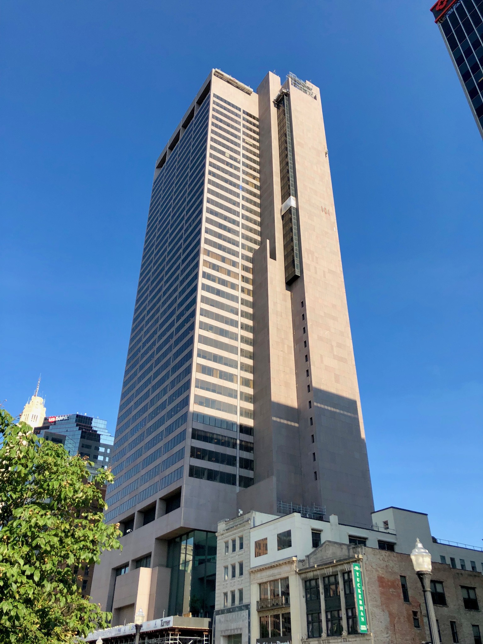 Tall brown modernist skyscraper rising into a clear blue sky above historic low-rise storefront buildings in downtown Columbus.