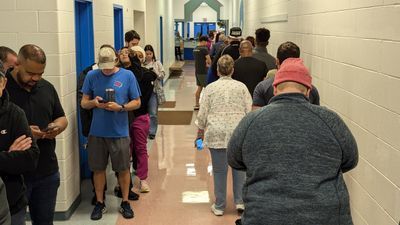 A long queue of voters standing in a white hallway with blue door trim waiting to vote.