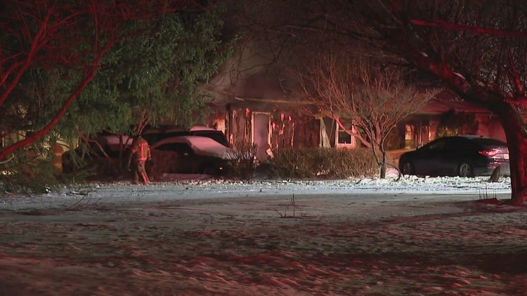 Charred facade of a single-story house with heavy burn marks, bare trees, snow-covered cars, and emergency personnel in Pataskala.