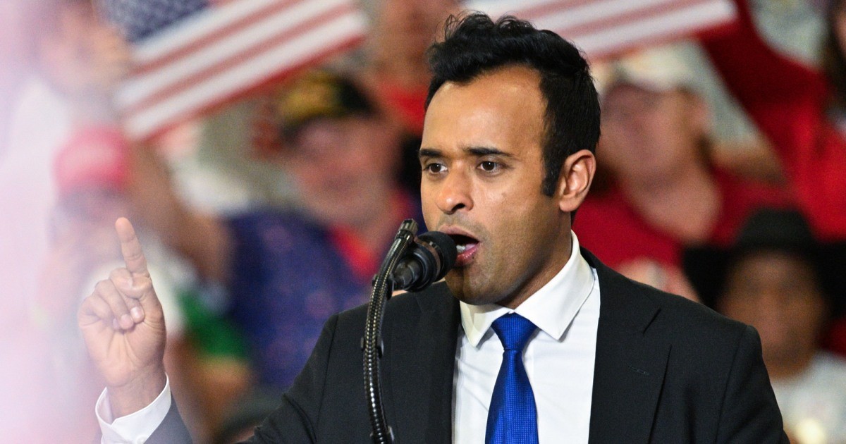 Vivek Ramaswamy speaking into a microphone with his right index finger raised in front of an audience.