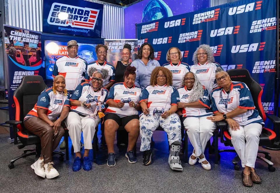 Group portrait of senior esports players wearing Team USA jerseys holding controllers, with Dr. Melita Moore standing in the back row.