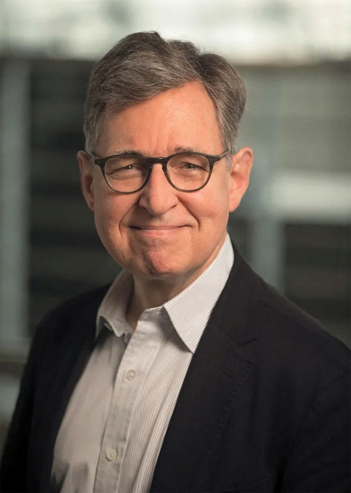 Color headshot portrait of economist Michael Woodford wearing dark-rimmed glasses, a button-down shirt, and a dark blazer.