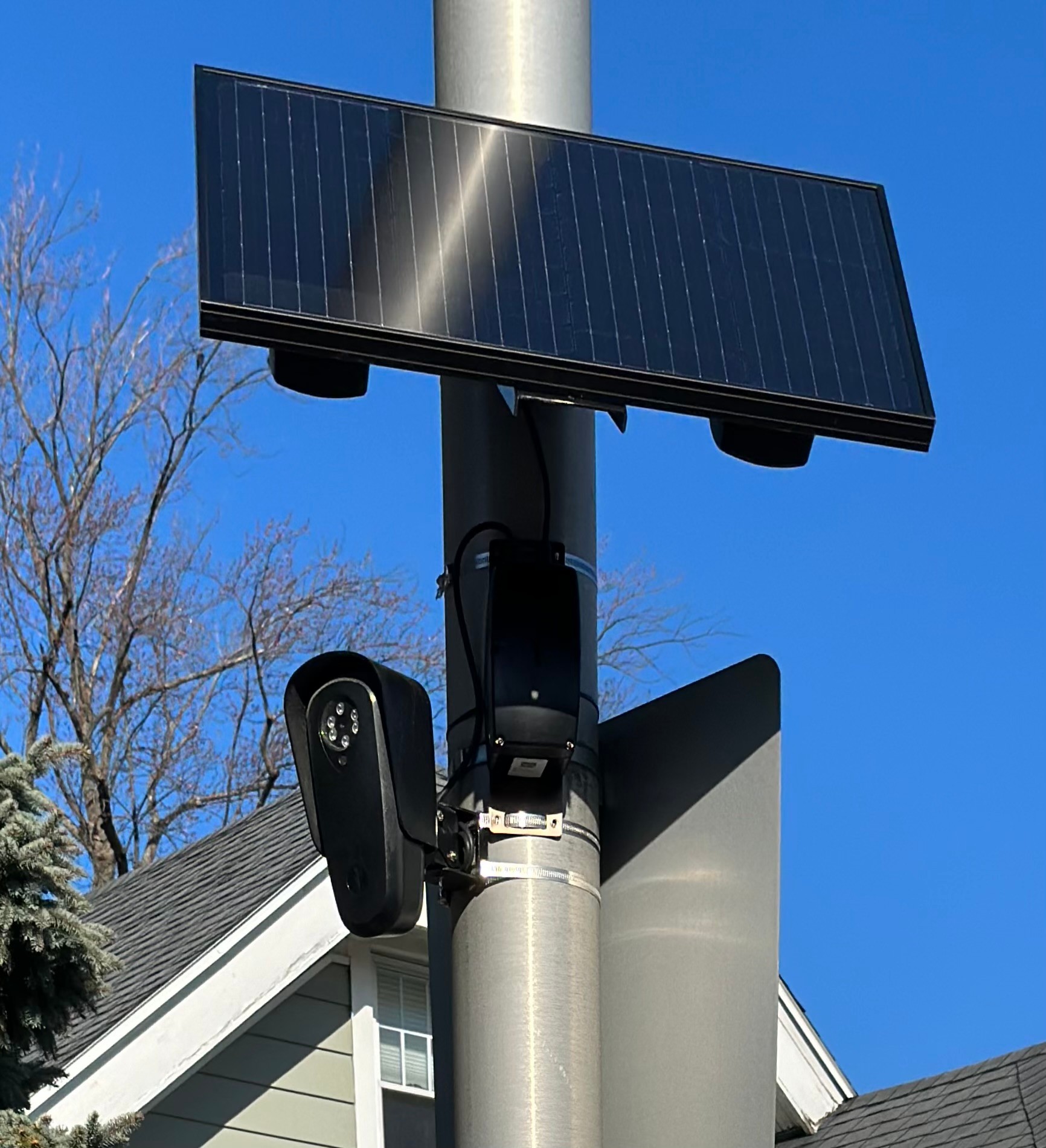 A pole-mounted Flock Safety automated license plate reader camera with a solar panel against a blue sky.