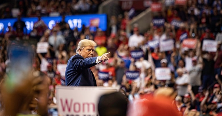 Donald Trump gestures forward from a podium while addressing an indoor campaign rally.