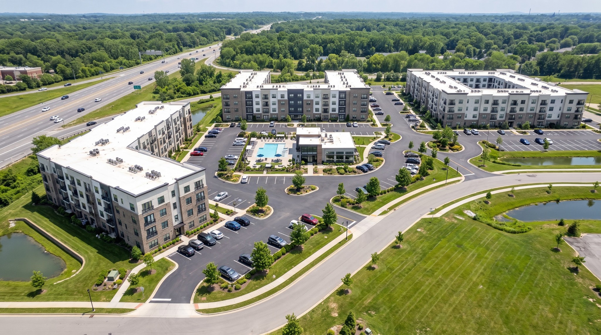 Oblique aerial rendering of three four-story apartment buildings, a central clubhouse, and surface parking.